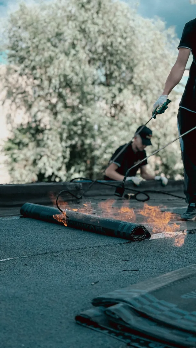 Roofer applying torch-down waterproofing membrane